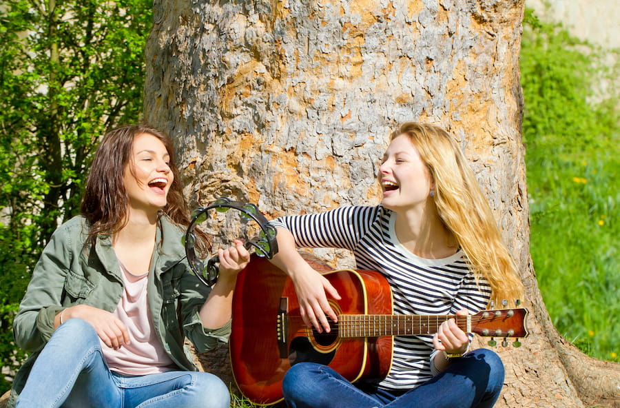dos chicas tocando la guitarra , la pandereta y cantando
