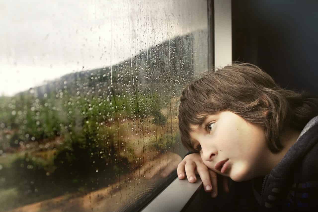 niño triste mirando la lluvia a través de una ventana